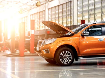 Ein orangefarbenes SUV steht in einer gut beleuchteten Auto-Werkstatt bei Autoankauf Wedel, dessen Motorhaube offen ist und den Motor zeigt.